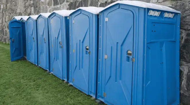 Row of blue portable toilets lined up on grass against a stone wall for event sanitation in Gilbert, AZ